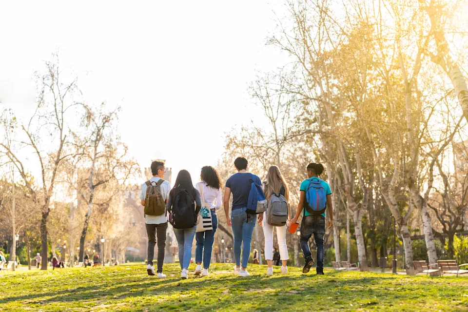 Group of travelers with backpacks walking through a park, enjoying a sunny day and nature