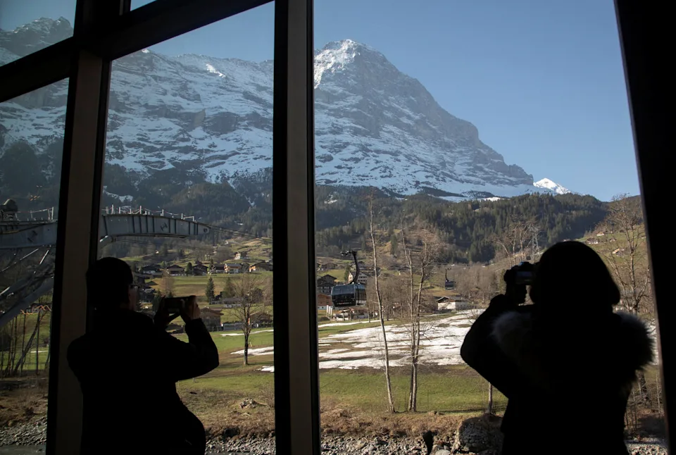 Tourists take pictures of the north face of Mount Eiger through a window of the terminal of the Eiger Express cable car in the Alpine resort of Grindelwald, Switzerland on April 14, 2022.