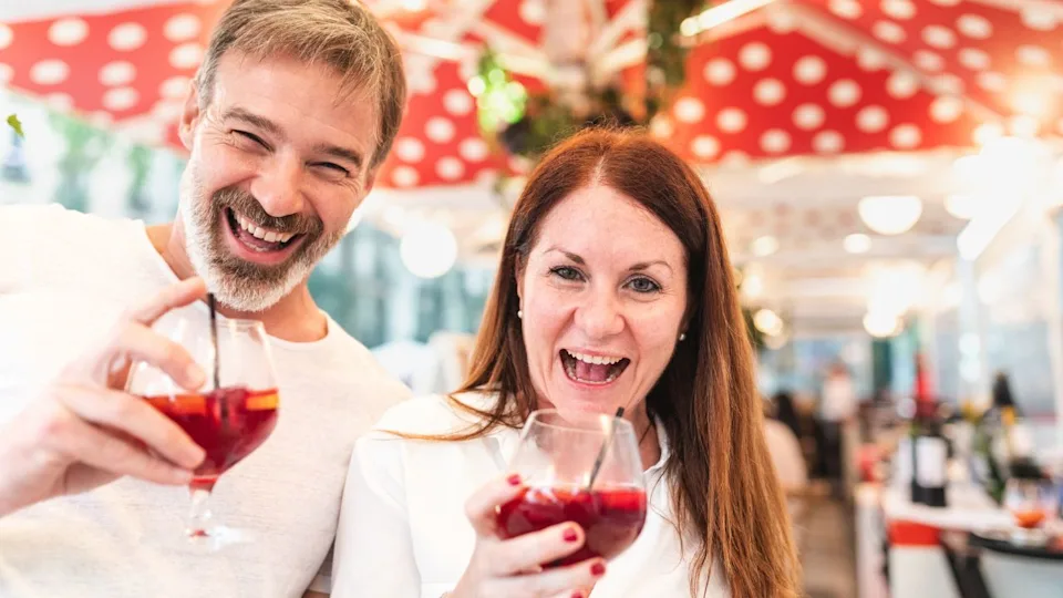 Happy people couple or friends enjoying a drink in Barcelona and laughing - Adult man and woman together at a bar in Barcelona enjoying a glass of sangria and having fun - Love and lifestyle concepts