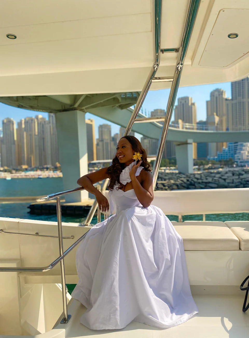 I sat on a yacht in Dubai Marina wearing a white dress and a floral hair accessory with the city skyline in the background.