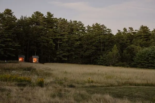 The tiny, open sleeping shelters abut a stand of woods. Their open fronts frame views of the Wanderwood farm.