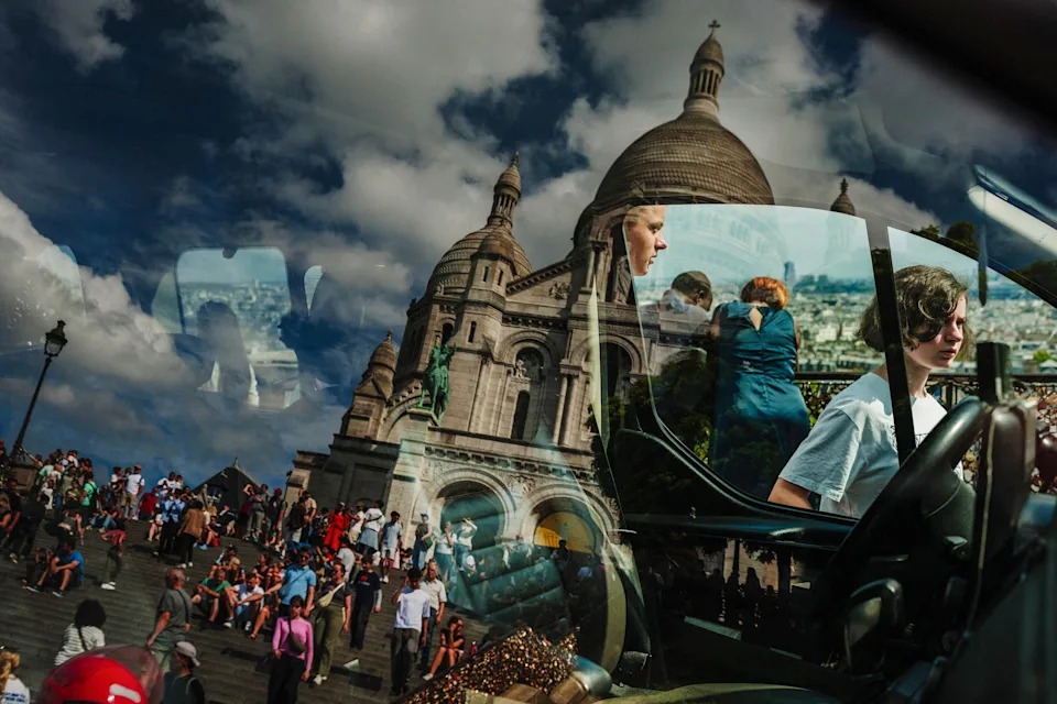 The Sacre-Coeur Basilica is seen reflected in a glass of a taxi as tourists stroll on the Montmartre hill of Paris, on August 1, 2025.