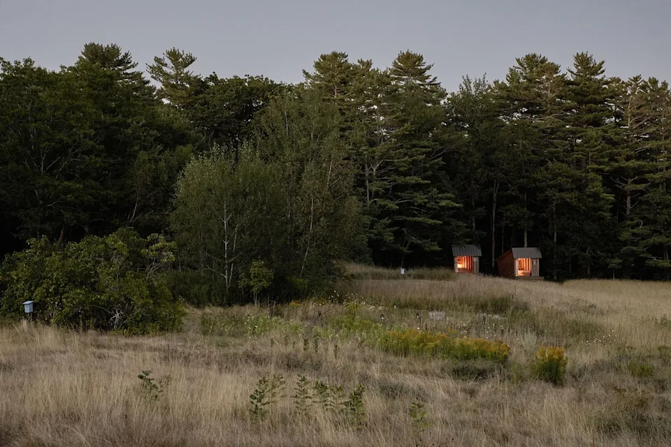 The tiny, open sleeping shelters abut a stand of woods. Their open fronts frame views of the Wanderwood farm.