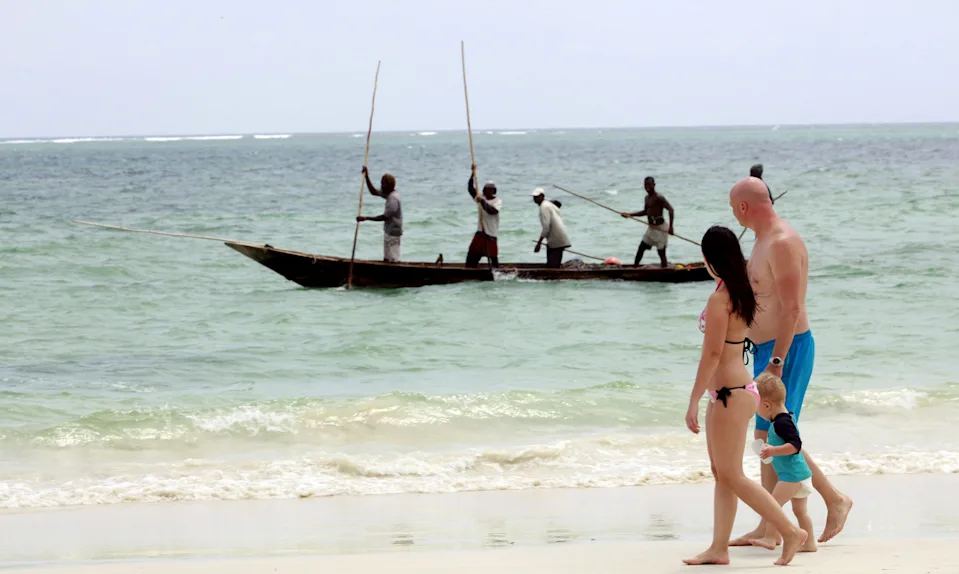 Tourists walk along the beach as fishermen paddle their boat near the shores of the Indian Ocean in the Kenyan coastal city of Mombasa, Jan. 18, 2016.