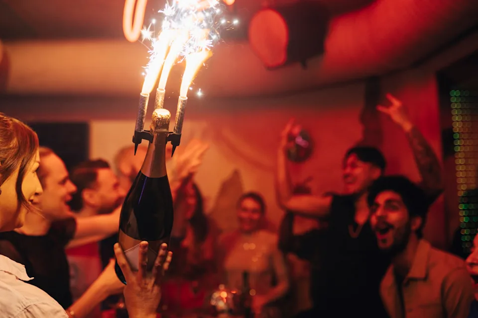 People celebrating indoors with sparklers on a champagne bottle, indicating a lively party or event
