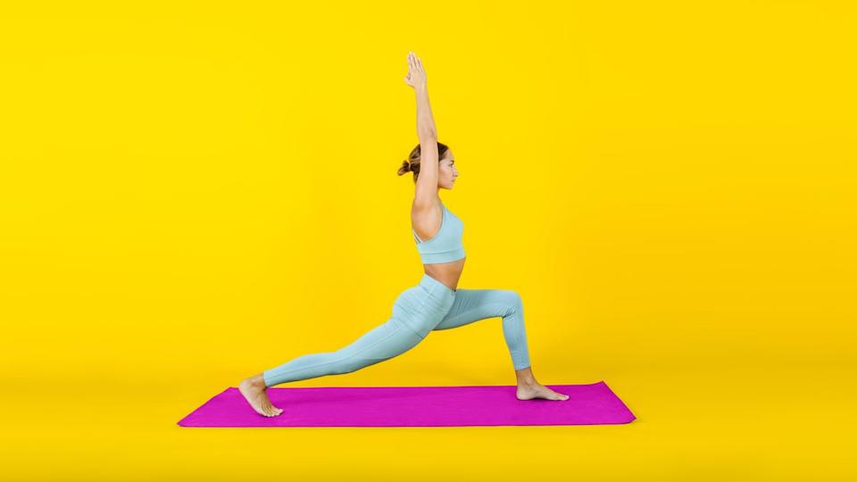 Woman holding a lunge while on a pink exercise mat in a bright yellow room.