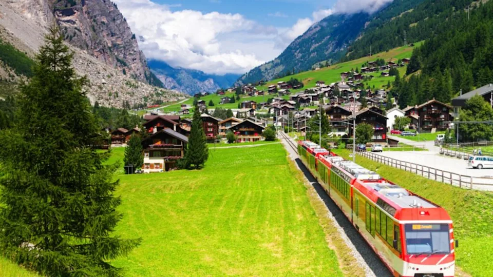 Red (glacier express) train heading through high mountain valley in switzerland alps on route from St. Moritz to Zermatt