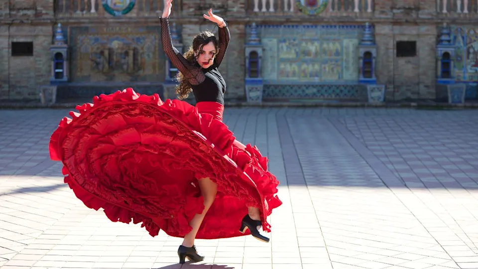 Beautiful woman dancing flamenco in a square in Seville, Spain. She is wearing a typical red and black gypsy dress and dancing flamenco with a lot of art. Flamenco, cultural heritage of humanity