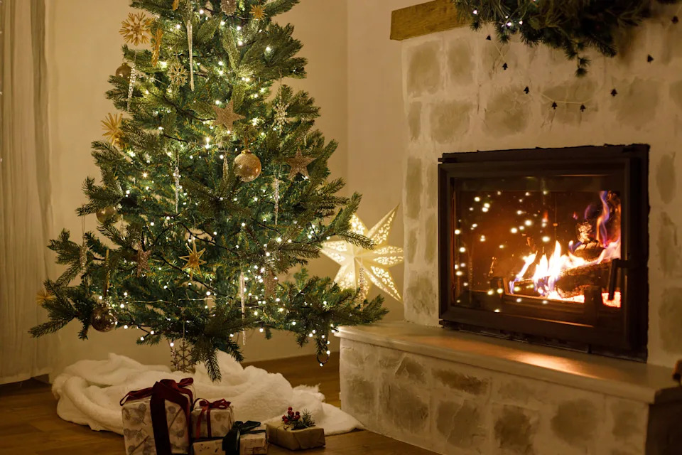 Stylish decorated christmas tree with vintage ornaments and modern decor of fireplace mantel with bells, ribbon and garland lights in evening. Atmospheric christmas eve at home. Merry Christmas!