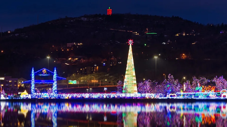 colorful christmas lights display seen at a distance along the water, which reflects them with a giant light display in a christmas tree shape at one end and lir trees and displays leading up to it