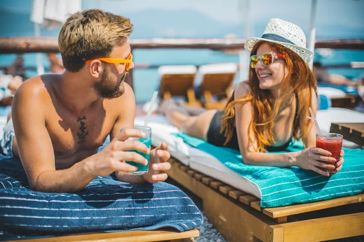 Couple having drinks on beach loungers.