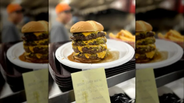 A green chile cheeseburger with four burger patties in a restaurant kitchen window
