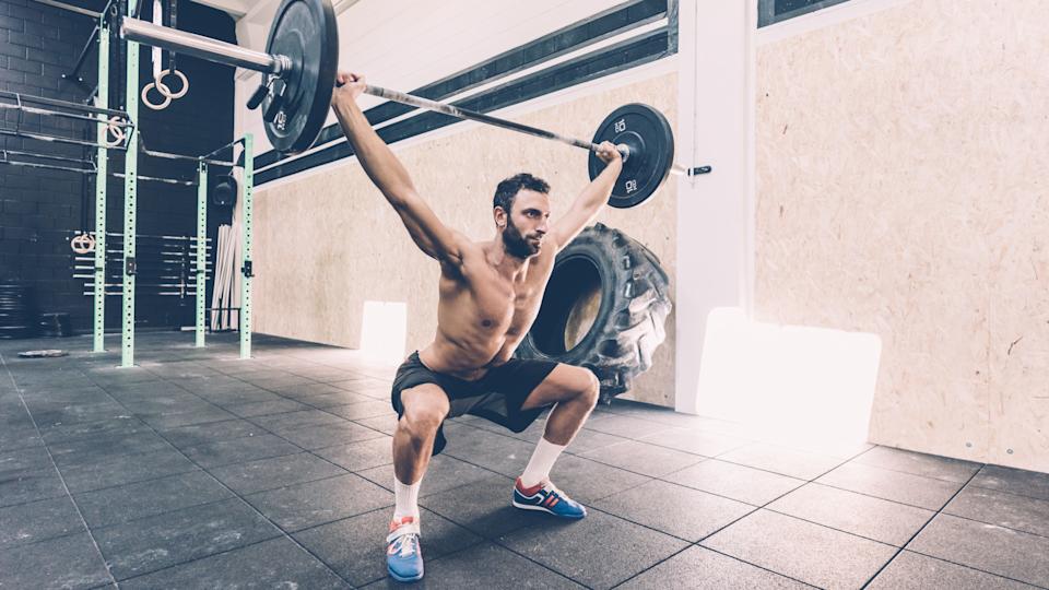 Man performing a snatch exercise holding a barbell in an overhead squat position in a gym 