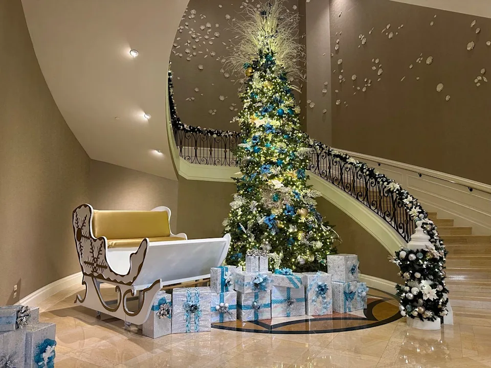Spiral staircase with garland and large, light-covered tree in front of it