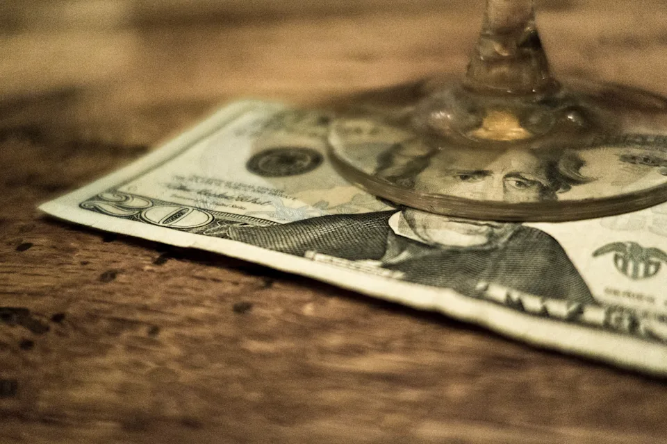 Close-up of a glass resting on a 20-dollar bill on a wooden table surface