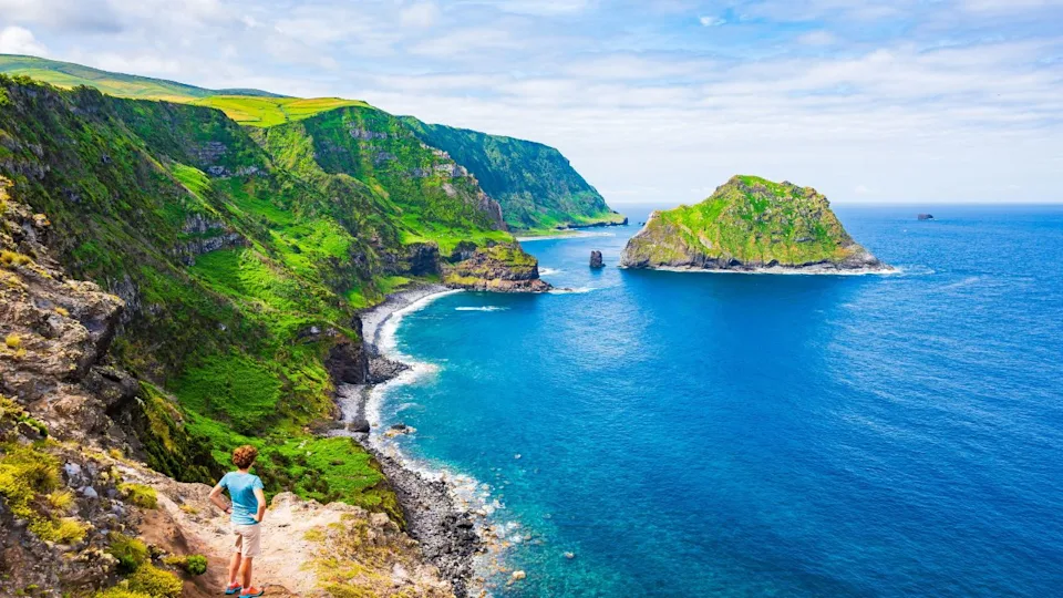 Young woman tourist looking at beautiful bay with beach and green cliffs at Baia de Alem, Flores island, Azores, Portugal