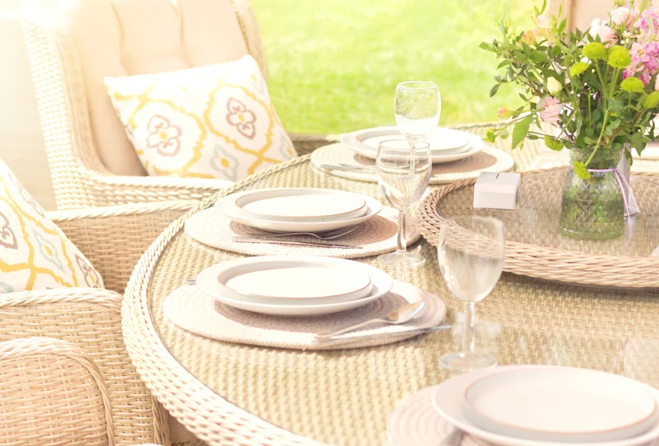 Wicker outdoor dining set with four place settings, wine glasses, and a vase of flowers. Bright and inviting casual elegance