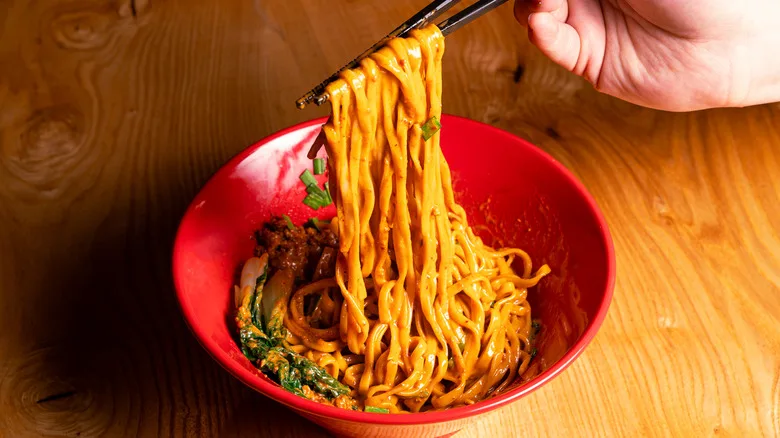 Close-up image of one of the soupless ramen dishes, and a person's hand holding chopsticks and picking up the noodles, at Akahoshi Ramen.
