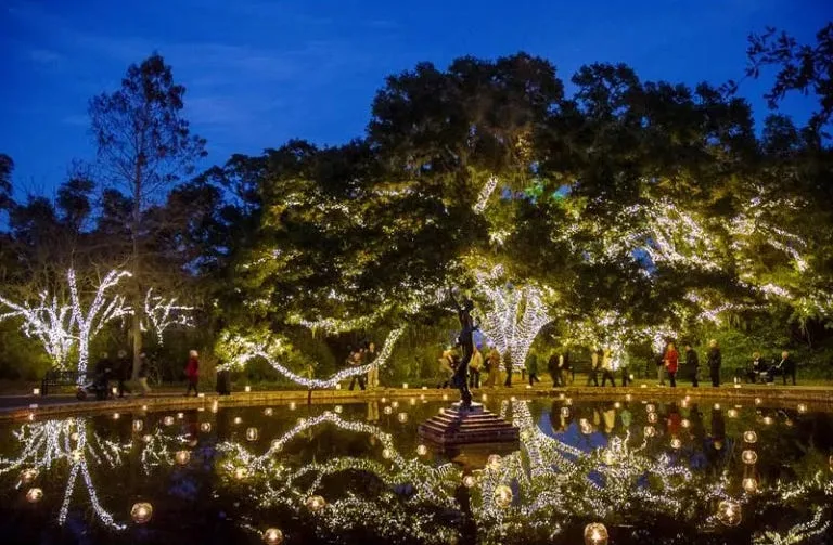 garden decorated with white lights and candles featuring a reflecting pond in foreground with a statue and trees behind it