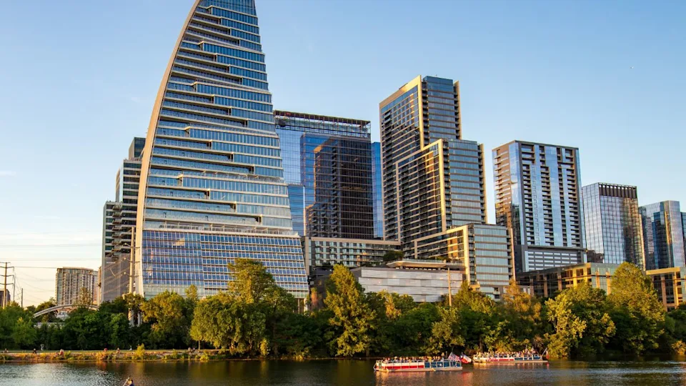 Modern architecture and high-rise buildings of Austin, Texas with summer sunlight reflections on Lady Bird Lake. A ground-level view of the lake and boats on the water.