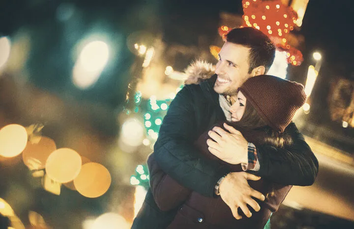 Couple having a cuddle looking at Christmas lights winter evening.