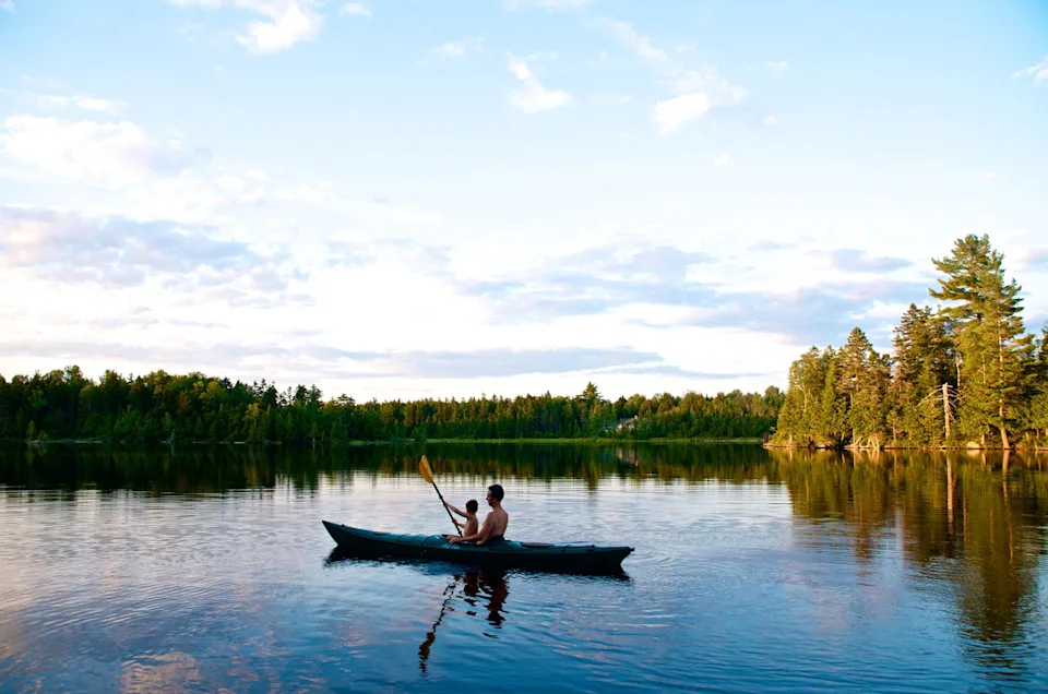 A man and his son kayaking on a serene lake.