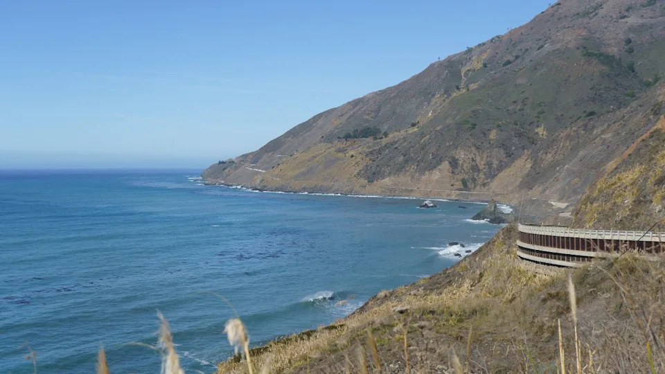 A scenic view of the Pacific Coast Highway as it winds along the rugged, sun-drenched cliffs of Big Sur, California.