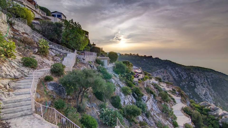 Sunrise timelapse aerial view of medieval houses from the top of the town of Eze village on the French Riviera early morning. Green trees and cloudy sky