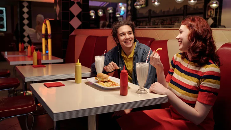 A couple smiling and eating fries in a diner