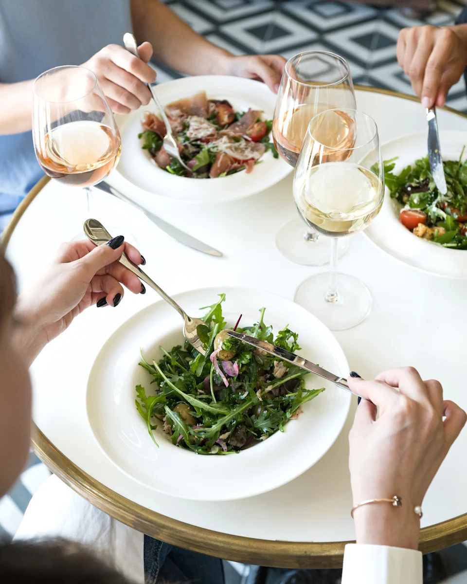 People dining at a round table with salads and wine, suggesting a travel or culinary experience