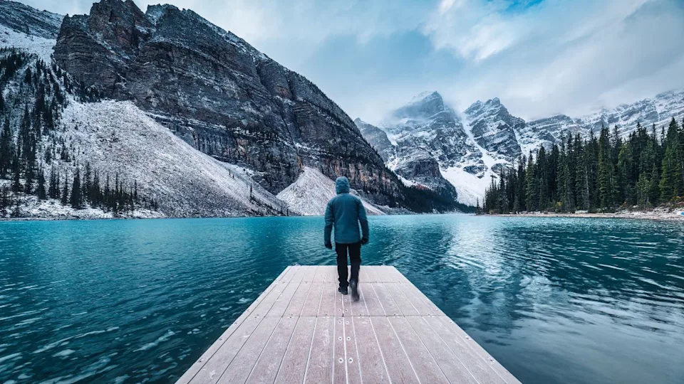 Lonely traveler man walking on pier surrounded by Rocky mountains on Moraine Lake at Banff national park, Alberta, Canada