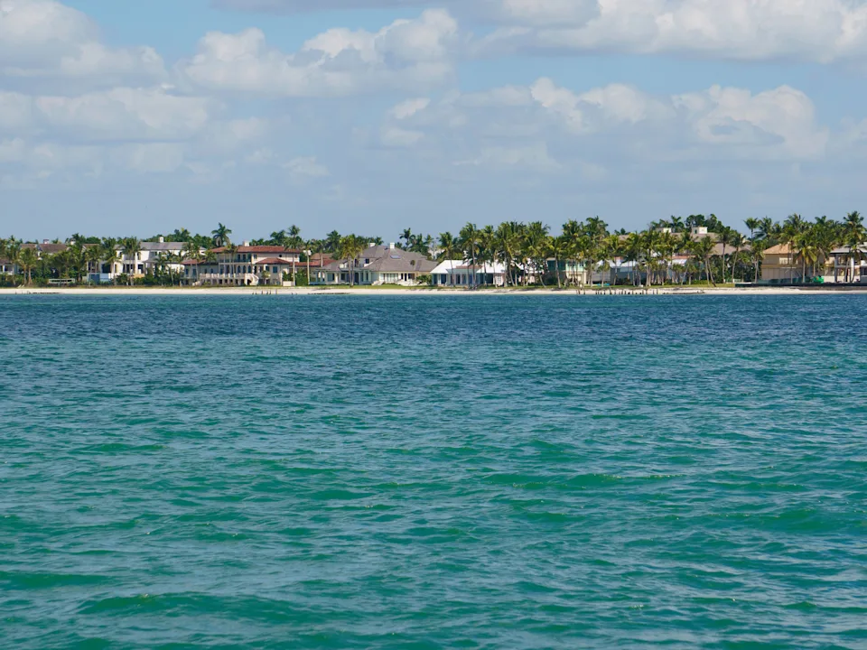 Blue ocean waters in front of a shore lined with homes and palm trees in Naples, Florida