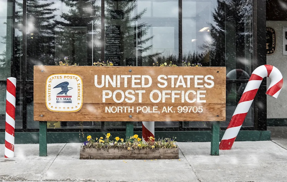 The North Pole, Alaska post office sign decorated with candy cane poles and snow falling during the holiday season.