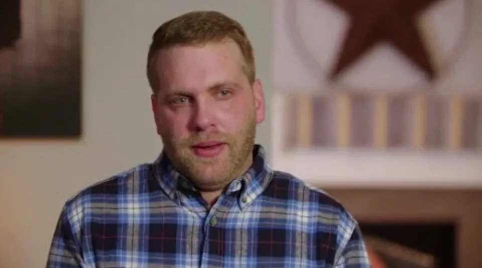 A person wearing a plaid shirt is indoors with a blurred background featuring a star-shaped decoration