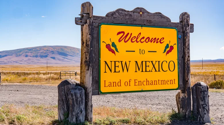 A rustic "Welcome to New Mexico" sign with chile peppers in front of desert mountains