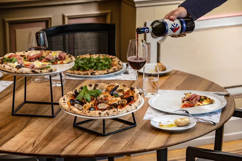 The Leading Hotels of the World Waiter pouring wine surrounded by pizza at Ristorante e Pizzeria Sapori.