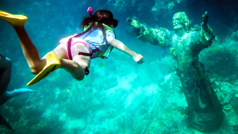 Girl snorkeling above a submerged statue of Jesus Christ