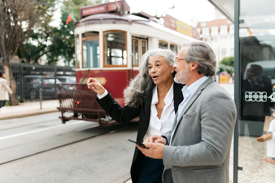 A retired couple stands near a Lisbon tram, exploring the city as they consider long-stay residency options in Portugal for warm-weather living.