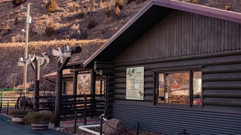 A dark wooden building, antlers on posts. an arid mountain in the background