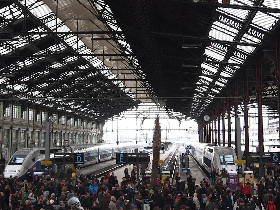 Crowded train station with high glass ceilings, multiple platforms, and people gathering, suggesting a busy travel hub