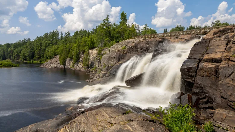 Waterfall cascading over rugged rocks into a river, surrounded by lush green trees near Bracebridge