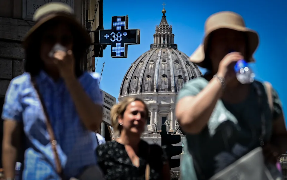 This photograph shows a pharmacy sign indicating the current outside temperature of 38
degrees celsius, with the dome of Saint Peter's Basilica in the background.