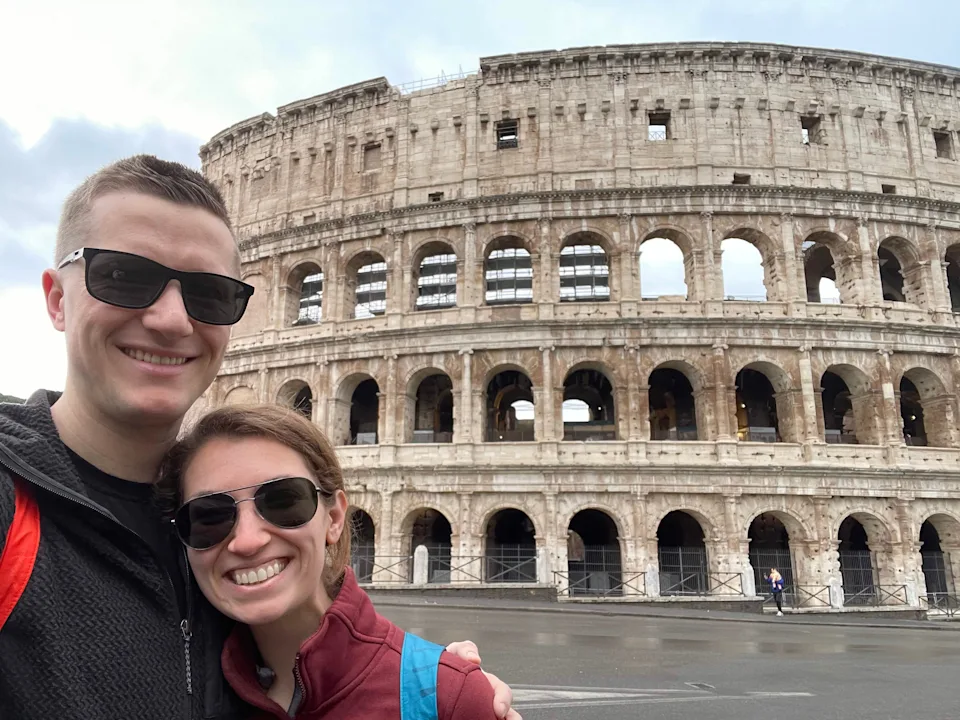 Maria Laposata and her husband wearing sunglasses and standing with Rome's Colosseum in the background.