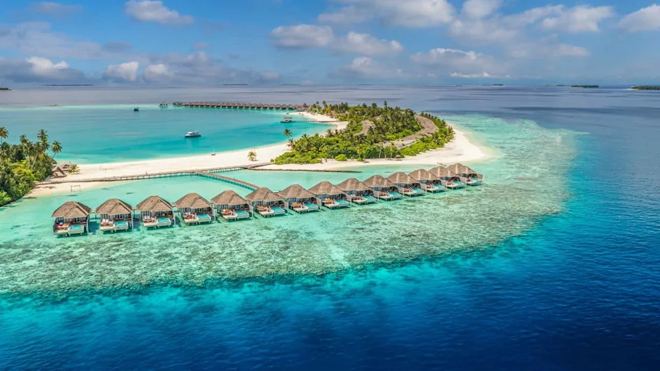 Amazing aerial view of Maldives island resort turquoise lagoon overwater villas white sand beaches lush palm trees, serene ocean view. Perfect tropical paradise escape, best tourism vacation wallpaper