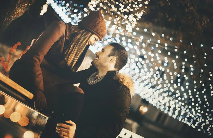 Couple winter night having fun while taking a walk. They are having a sincere laugh with many glittering Christmas lights around them.