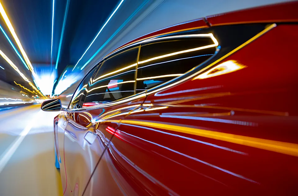 Sleek red car speeding through a tunnel with blurred light trails, suggesting motion and modernity. Ideal for Work & Money themes