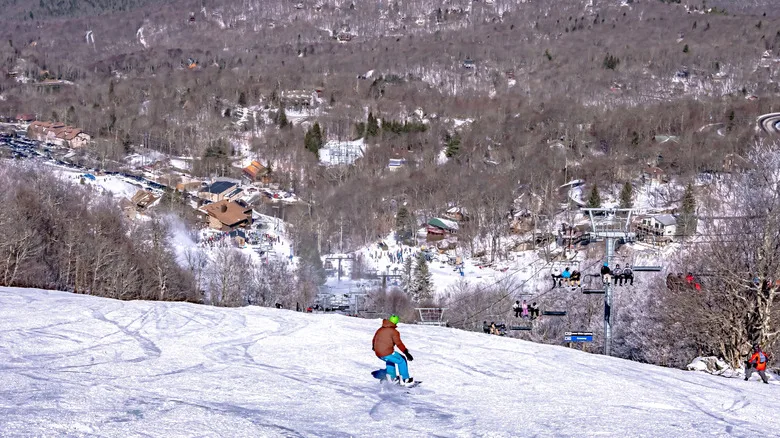 People skiing and snowboarding down a slope overlooking resort cabins at Beech Mountain, North Carolina