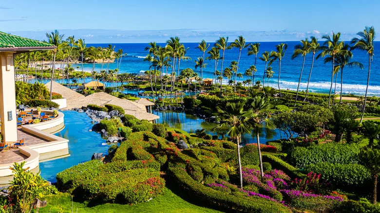 A luxury resort with palm trees, pools, gardens, and villas overlooking the ocean in Hawaii