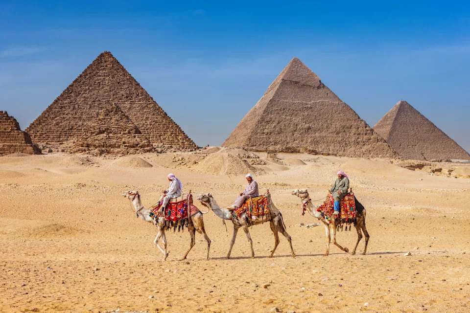 Bedouins riding on camels, pyramids on the background, Giza, Egypt.