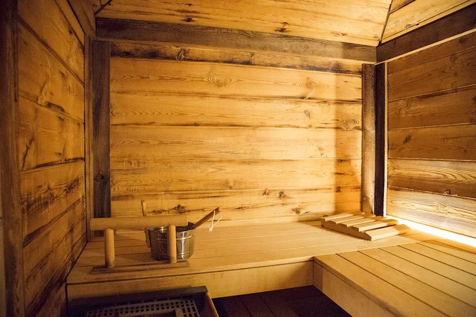 Wooden sauna interior with bench, bucket, and ladle on one side, providing a relaxing atmosphere